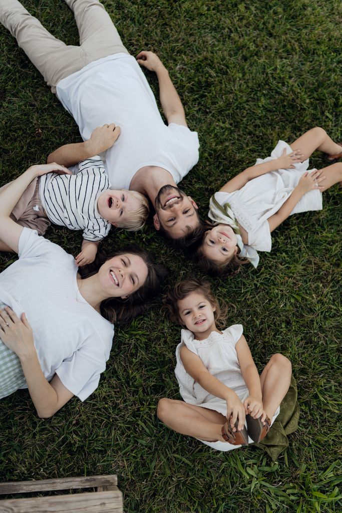 Joyful family of five relaxing on grass, enjoying a sunny day outdoors together.